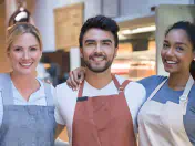 Happy people with aprons stand in front of a cafe counter.